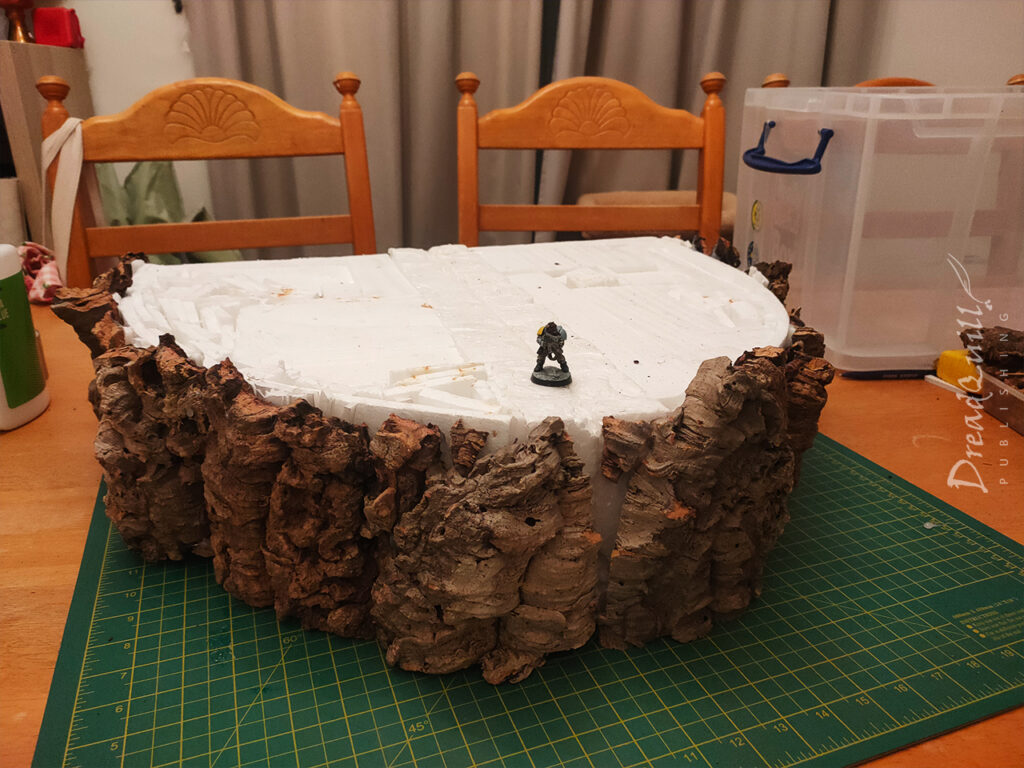 WIP ash waste modular hills, assembled from polystyrene and a raw cork bark face, with a 28mm miniature on top for scale